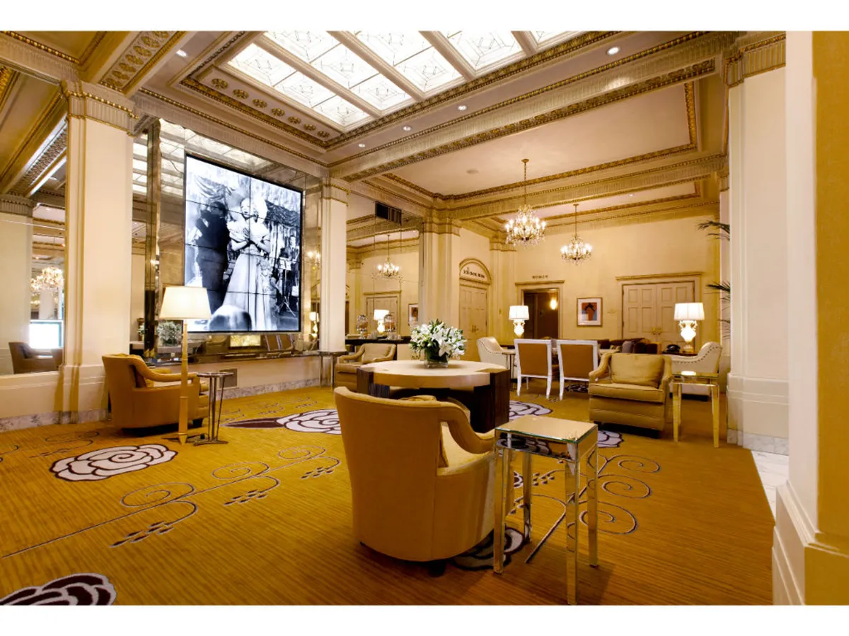 A sophisticated lounge area featuring a large screen displaying a historical image, a central coffee table, and luxurious seating. The scene is ideal for social gatherings and reflects a sense of upscale comfort and connection to the building’s history.