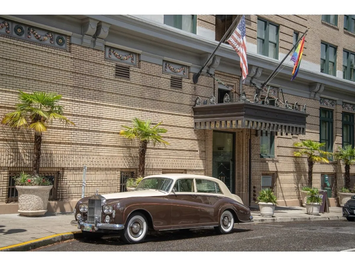 The elegant exterior of a historic building, complete with palm trees, flags, and a classic car parked at the entrance. Guests are seen arriving, hinting at the welcoming, sophisticated environment that awaits inside.