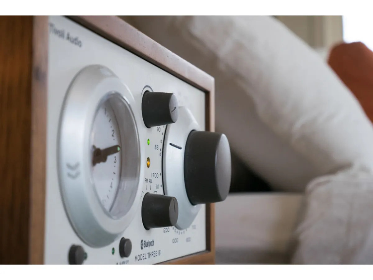 A close-up of a stylish Tivoli Bluetooth radio with chrome control knobs, set in a cozy suite environment. The scene exudes comfort, hinting at the enjoyment of music and tech comforts as part of the in-suite experience.