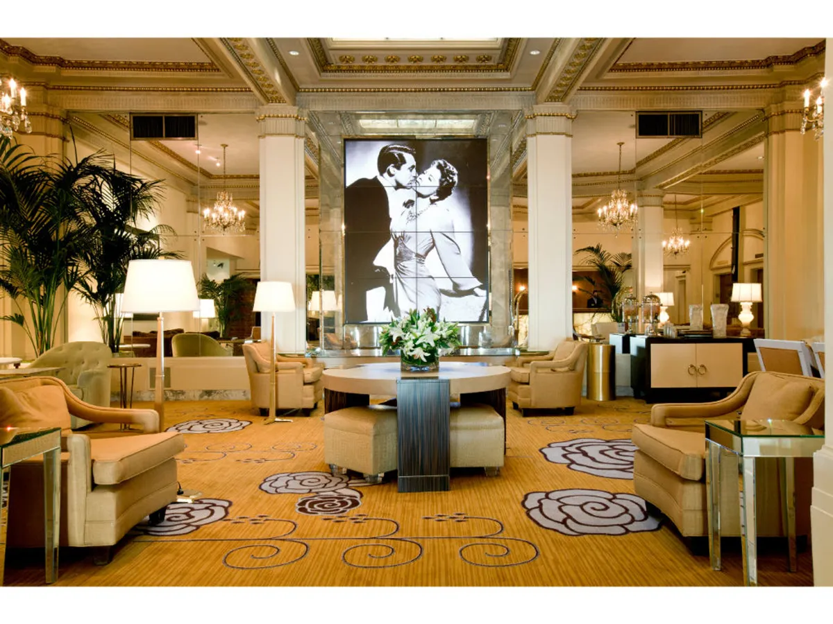 A sophisticated in-suite living area featuring plush seating, a prominent floral arrangement, and a large portrait of a dancing couple. The setting is both inviting and refined, ideal for relaxing or enjoying local treats from the mini-refrigerator.